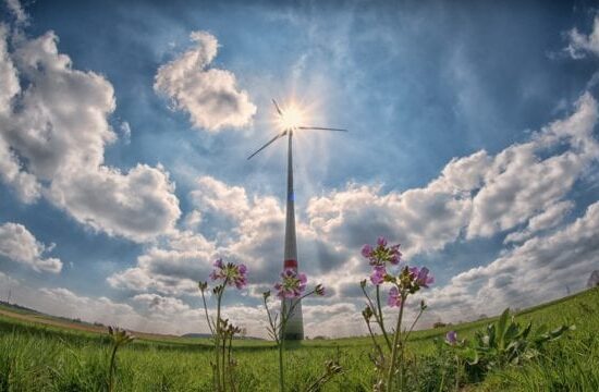 Aerogenerador al centro sobre un campo verde visto desde abajo con el cielo azul y nubes alrededor