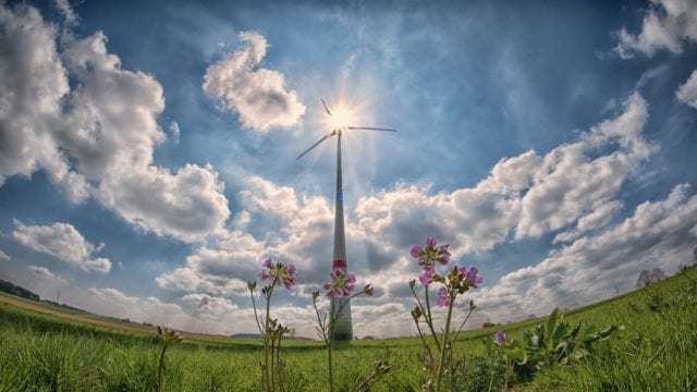 Aerogenerador al centro sobre un campo verde visto desde abajo con el cielo azul y nubes alrededor